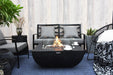 Backyard Lifestyles Modeno - Aurora Fire Table Square Black front view of fire table with flames and glass screen on a deck with patio furniture