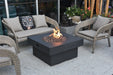 Backyard Lifestyles Modeno - Branford Fire Table in Black front angle view of fire table with lava rocks and flame on a deck with patio furniture